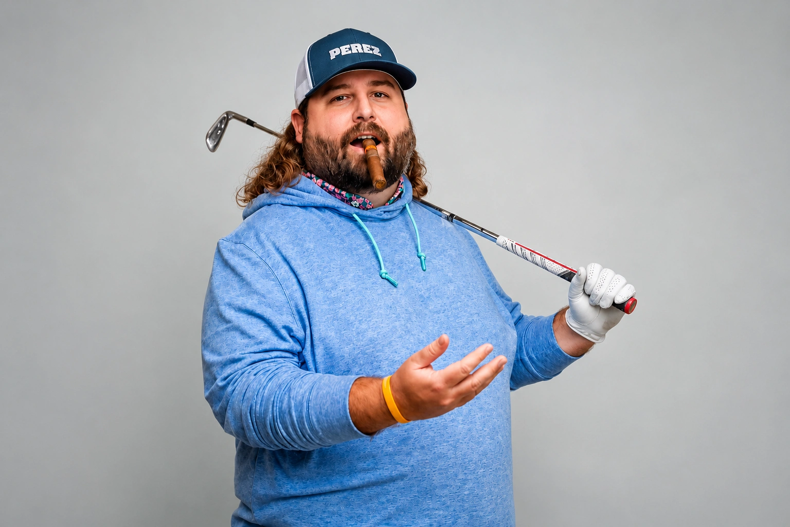 Man in a blue hoodie and cap holding a golf club over his shoulder while gesturing with his hand, showcasing a relaxed golfing attitude.