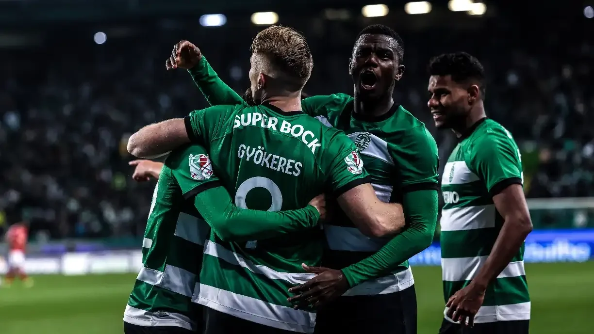 A group of soccer players celebrates a goal, raising their arms and smiling in a display of excitement and teamwork.
